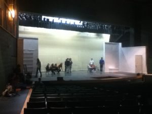 The cast mingle on stage as a microphone sound check takes place. The set (as of Wednesday, Jan. 22) was painted entirely white in preparation for the bright colors of the 1920s. The set features the narrator’s apartment, the Grand Hall, the groom’s room, the bride’s room, and an outdoor set with the appearance of a biplane. Photo courtesy of Tori Swart