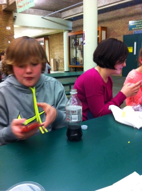 Freshman Ryan Tufts battles his friend as they sit side by side at lunch. The game has brought shouts of “It’s your turn” to the commons. Students also ask teachers and peers for help with difficult questions in the thirty seconds available to answer.  Photo courtesy of Jenna Bao
