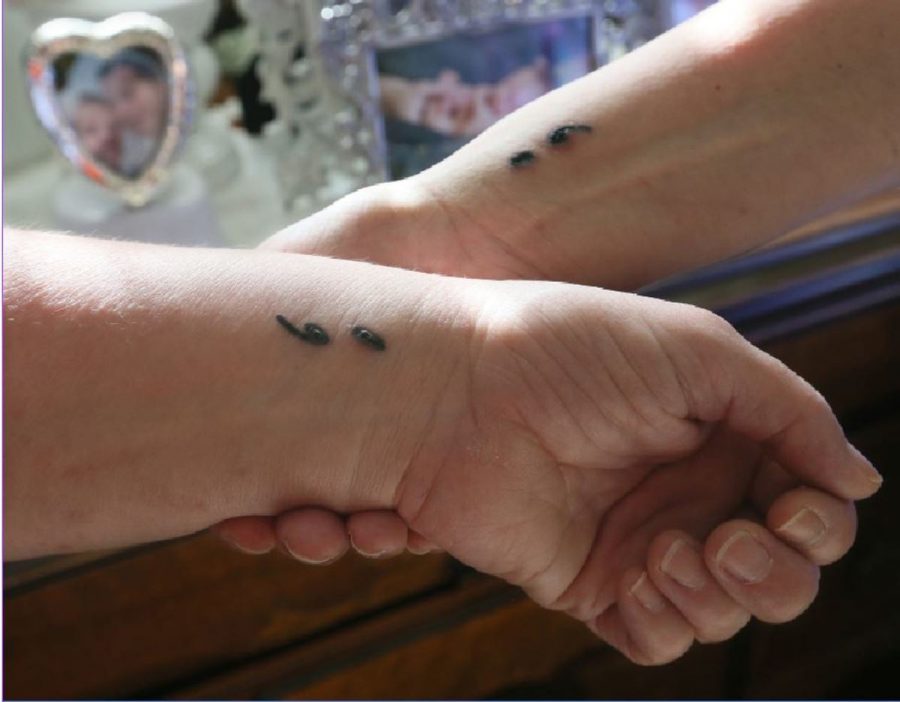 Two hands are shown with semicolons tattooed on their wrist. The semicolons remind them that their story is not over. The idea came from creator Amy Bleuel when she herself was struggling with depression.