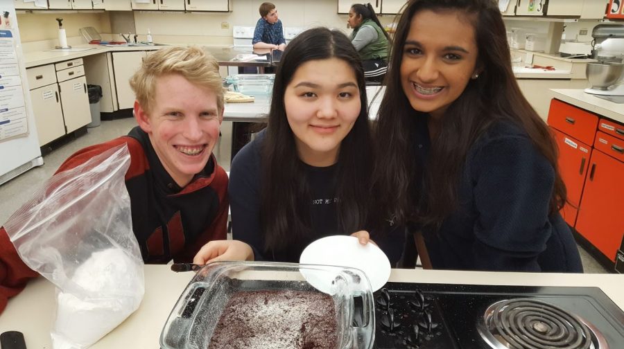 BAKE. Juniors (left to right) Adam Kossen, Alia Diushebaeva, and Eshika Kohli wait for their brownie to cool after pulling it out of the oven. At the last Colorful Eats meeting, vegan velvet brownies and strawberry cupcakes were made. Brownies were coated with a sprinkle of powdered sugar, and cupcakes were iced with vegan icing.