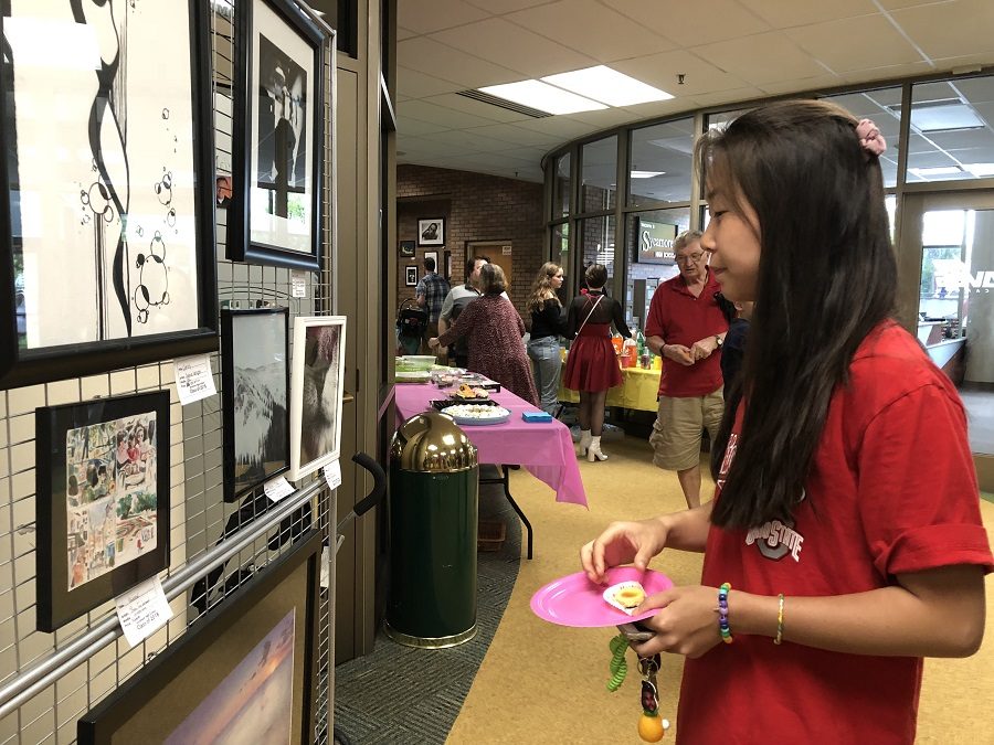 ART GALORE. Senior Kaitlyn Jiang looks at artwork on display at the Senior Art Show on May 4 as she snacks on some of the food provided. The show features pieces created by the AP Studio Drawing, 3D, and Photo seniors. This is their final show at the high school.