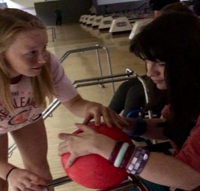 BOWLING CREATES BONDS. Freshman Lucille Clerc helps junior Ava Martin bowl. Martin uses a wheelchair, however she can bowl by pushing the ball down a ramp. She got the highest score in her lane on last week’s trip. Working with a peer in the bowling lane helps build valuable relationships between peers and Adaptive PE students. “I love being able to go to social events with [the special needs students] and have so much fun,” Clerc said.