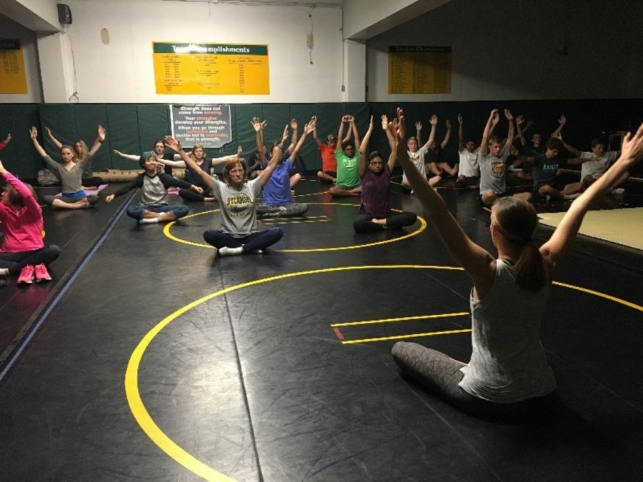 STRETCHING AWAY STRESS. Ms. Meredith Blackmore leads students and even a couple teachers in a yoga pose. At each meeting, students gather in the wrestling room and are led through a simple but effective yoga practice. The students learn how to breathe deeply and calm their bodies. “[Yoga is] good for [students’] mental health, it’s good for their physical health, and it’s good for their emotional health,” Blackmore said.