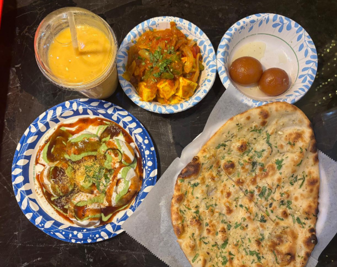 From top right clockwise: Gulab Jamun - sweet, soft, deep-fried spheres; Garlic Naan - Indian garlic-flavored flatbread; Dahi Puri - crispy hollows shells filled with potatoes, chickpeas, yogurt, tamarind chutney, and green chutney topped with crunchy chickpea flour noodles; Mango Lassi - yogurt-based mango smoothie; Kadai Paneer - Indian cheese cubes cooked in a tomato and onion based gravy mixed with cooked bell peppers.